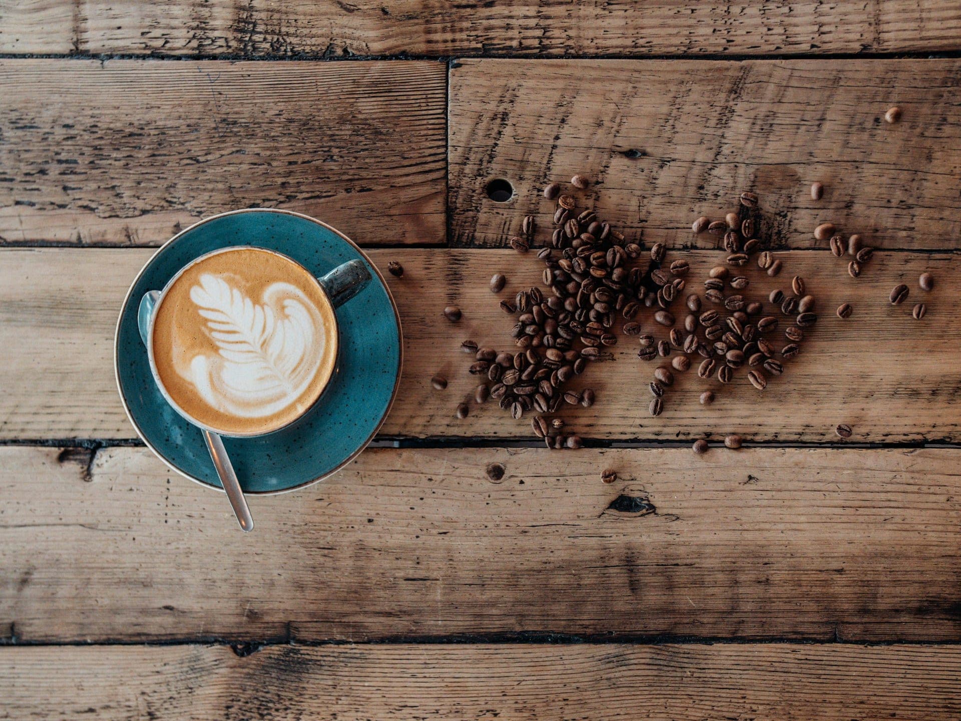 Cappuccino u plavoj šolji i zrna kafe na drvenom stolu